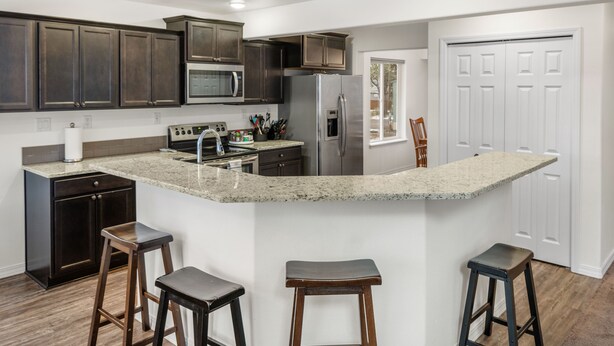 Una cocina con armarios de madera oscura, electrodomésticos de acero inoxidable, una encimera de granito y tres taburetes de bar.