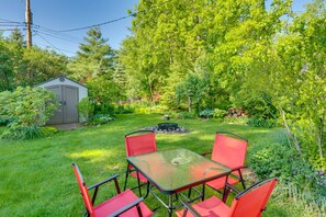 A patio with a glass table and red chairs, surrounded by lush greenery and a small shed. - Pet-Friendly Extended Stay Walk to Delavan Lake (Delavan)