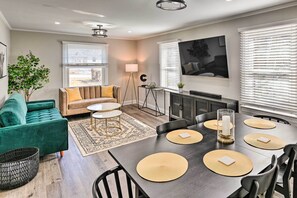 Una sala de estar moderna con un sofá verde, una mesa de comedor con individuales y un televisor grande en la pared.