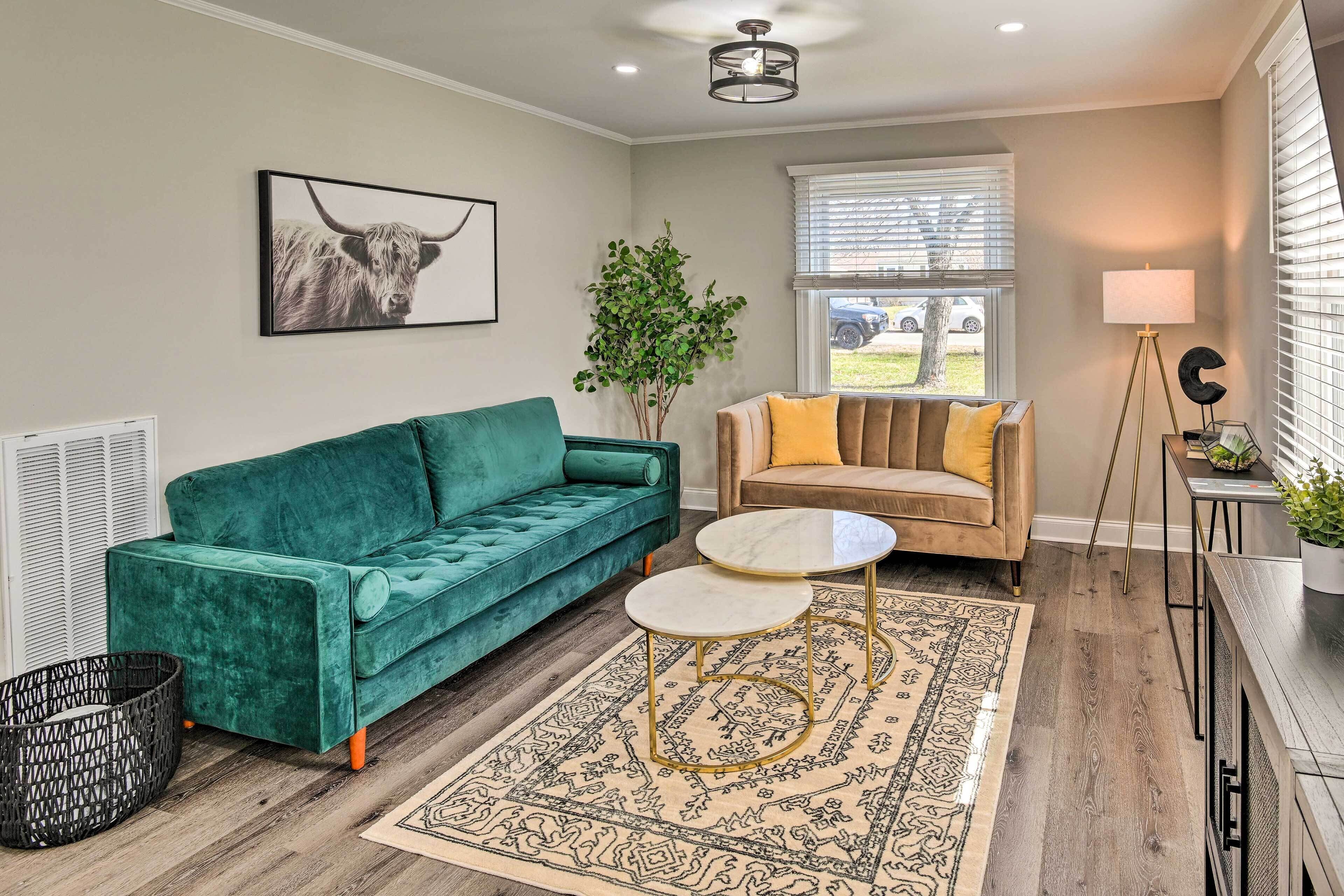 A living room with a green sofa, a beige sofa, a round table, a patterned rug, and a plant.