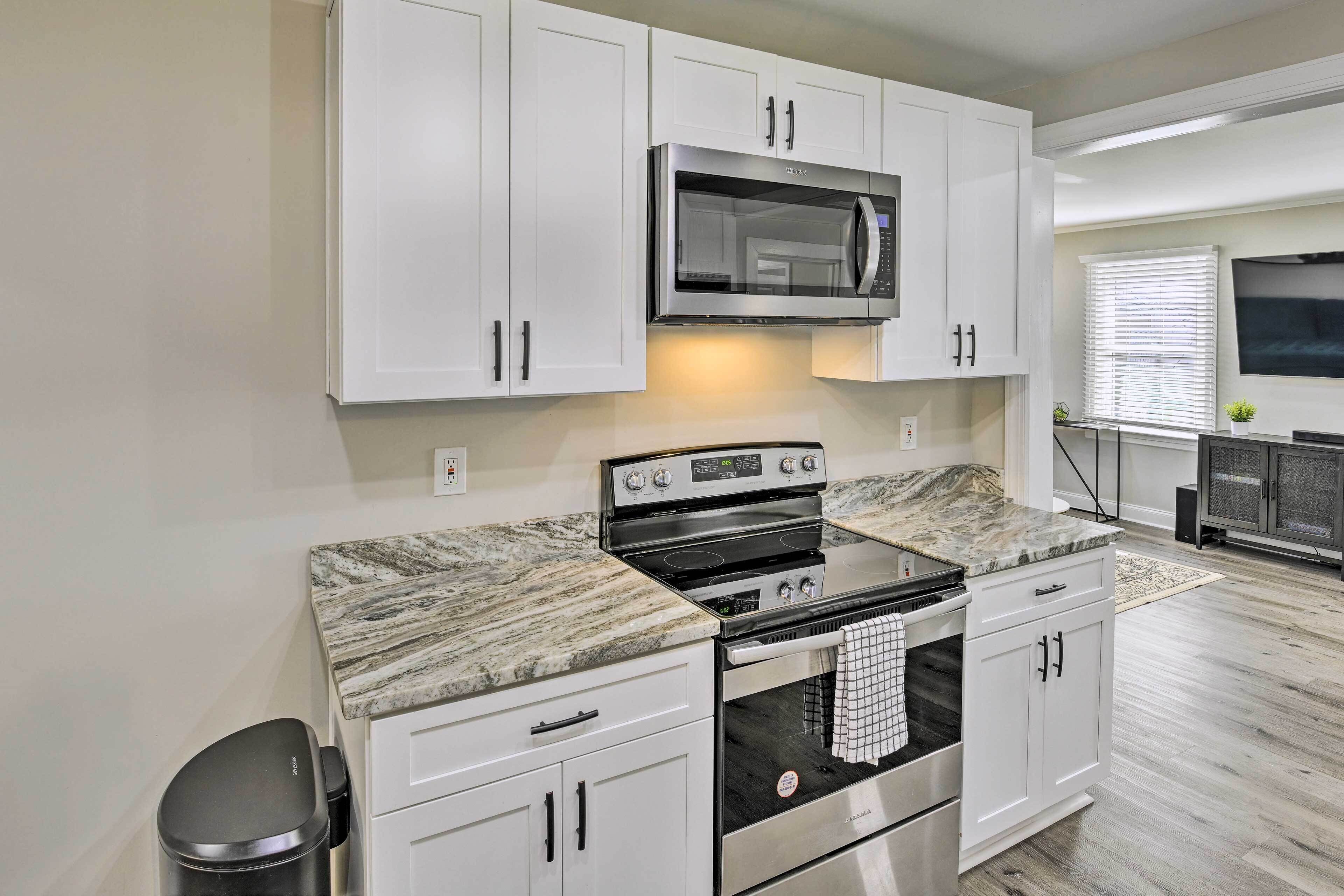 A modern kitchen with white cabinets, a stainless steel microwave, a black stove, and a marble countertop.
