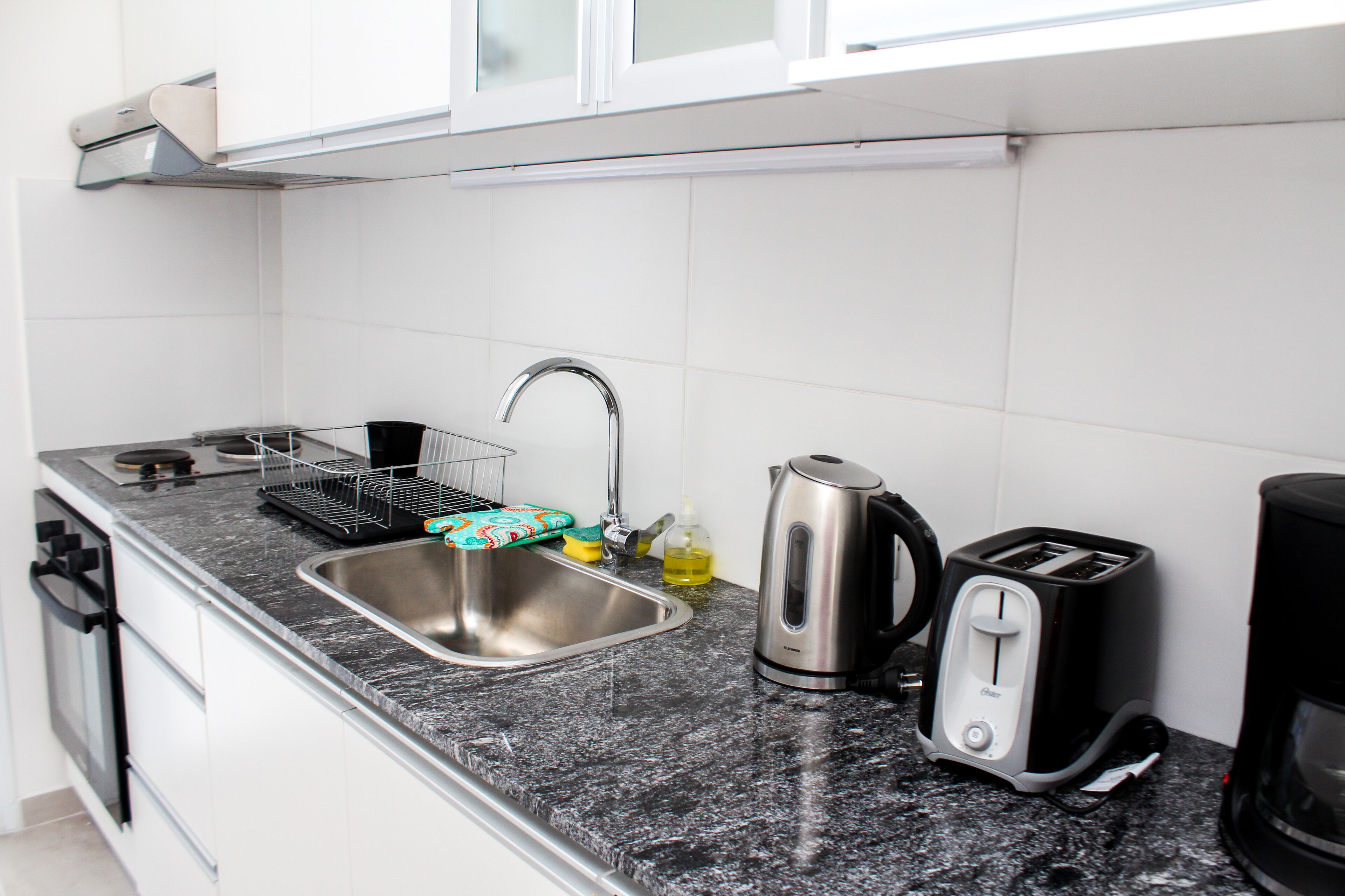 A kitchen with a stainless steel sink, a kettle, a toaster, and a coffee maker on a granite countertop.