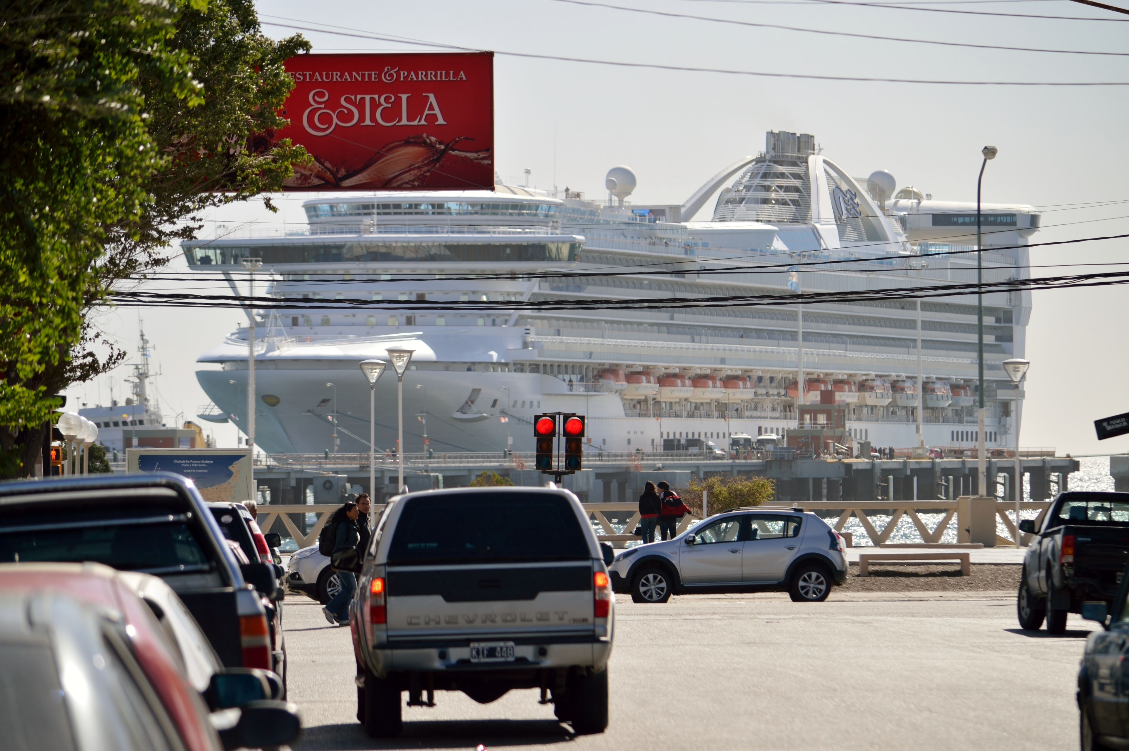 Une rue animée, avec un grand navire de croisière amarré au loin.