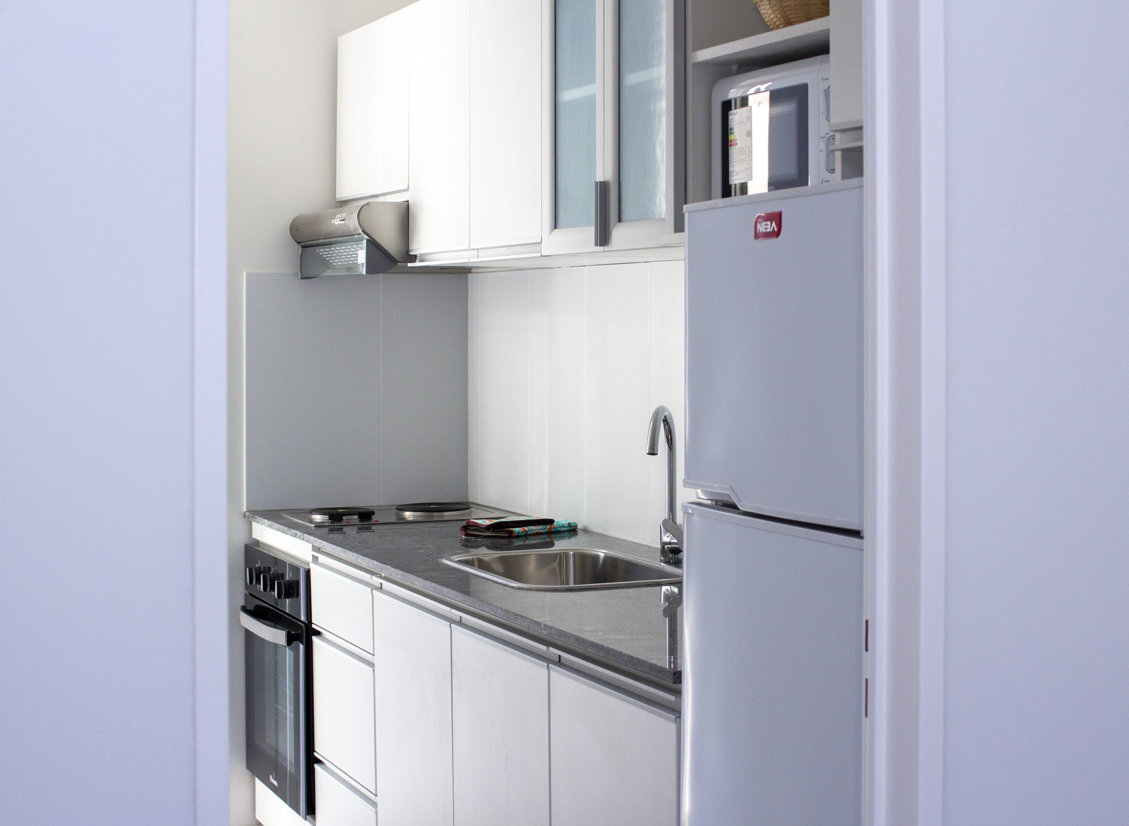 A modern kitchen with white cabinets, a stainless steel sink, a built-in oven, and a refrigerator.