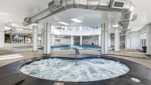 En stor inomhuspool med ett bubbelbad, omgiven av vita pelare och ett tak med synliga ventilationskanaler.