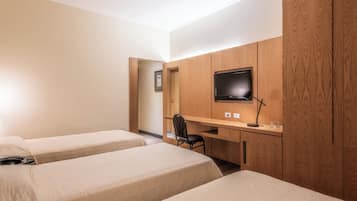 A hotel room with two single beds, a desk with a chair, a television, and wooden paneling.