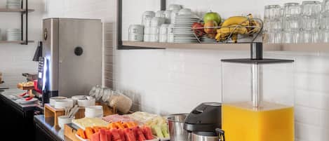 Um buffet de café da manhã com diversos tipos de comida, uma máquina de café e um dispensador de suco.