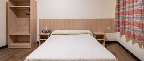Una habitación de hotel con una cama, un armario de madera, una mesita de noche con un teléfono y una cortina a rayas.