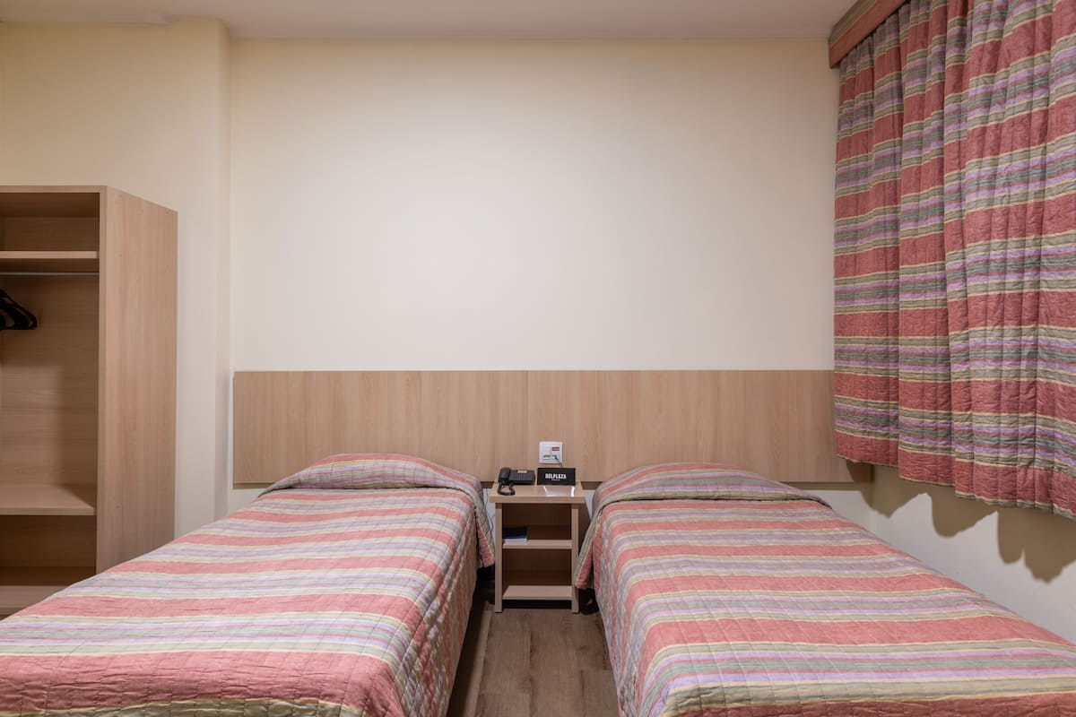 A twin room with two single beds, a wooden wardrobe, a bedside table with a phone, and a striped curtain.