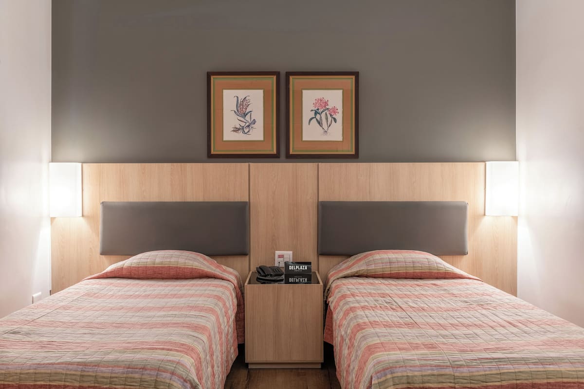 A hotel room with two beds, a nightstand, and two framed floral artworks on the wall.