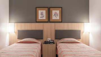Ein Hotelzimmer mit zwei Betten, einem Nachttisch und zwei gerahmten Blumenbildern an der Wand.