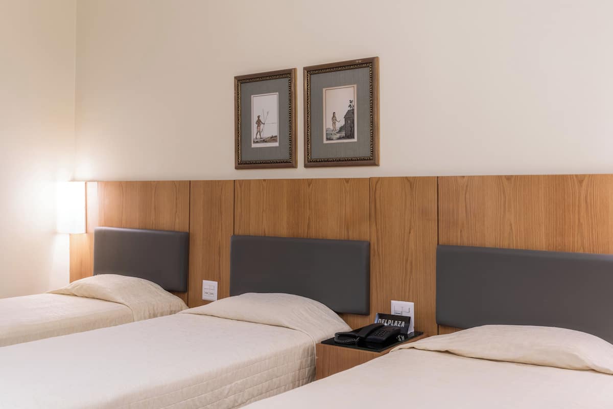 A hotel room with two single beds, a wooden headboard, a nightstand with a telephone, and two framed pictures on the wall.
