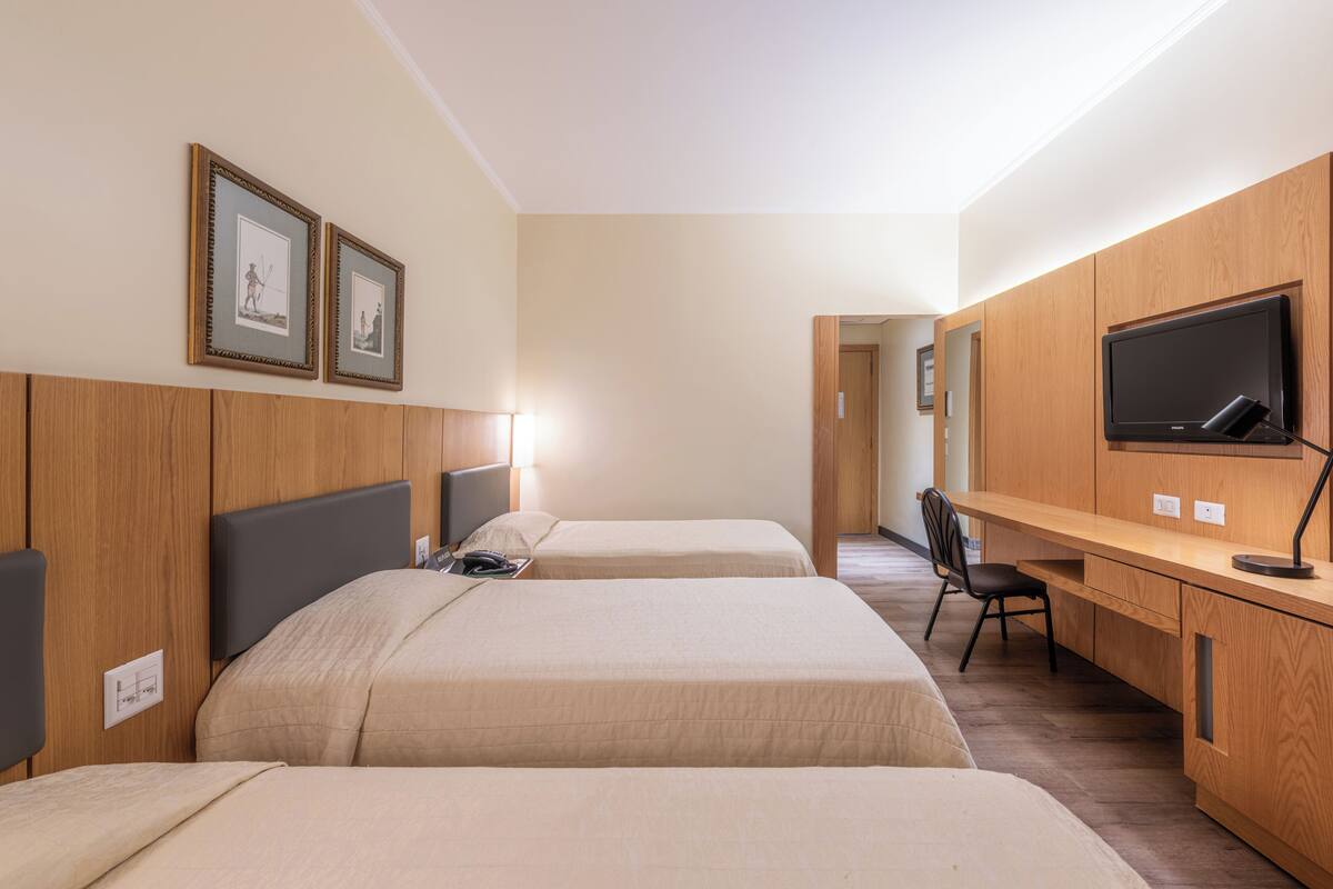A hotel room with two beds, a desk, a chair, a TV, and framed pictures on the wall.