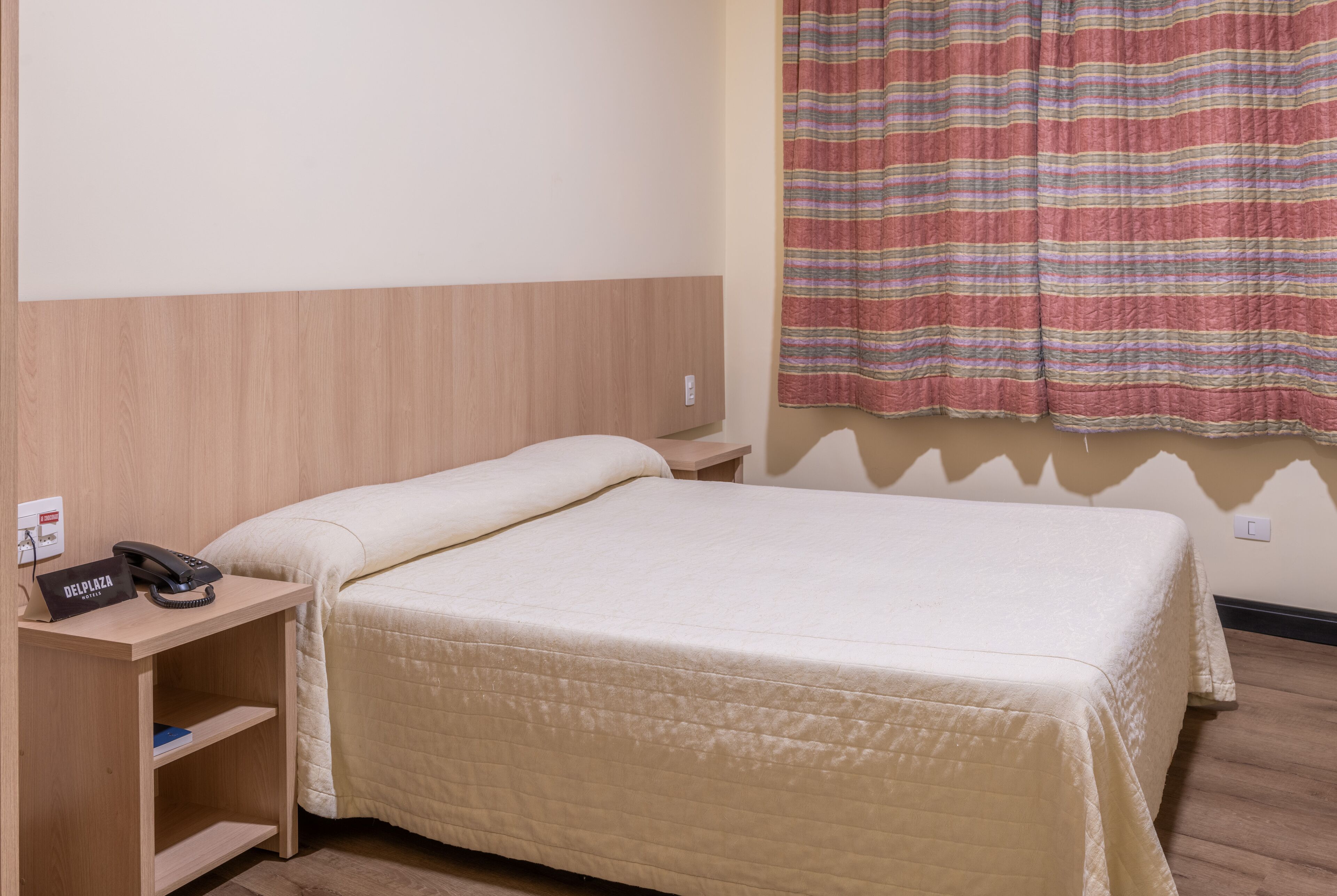 Une chambre d’hôtel avec un lit simple, une table de chevet avec un téléphone et un rideau à rayures.