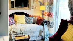 A cozy bedroom with a bed, a chair, a bedside table, and a window with curtains.