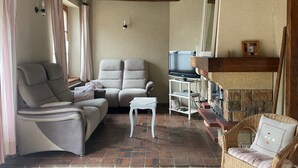 Un salon chaleureux avec un canapé, deux fauteuils, une petite table, un téléviseur et une cheminée.