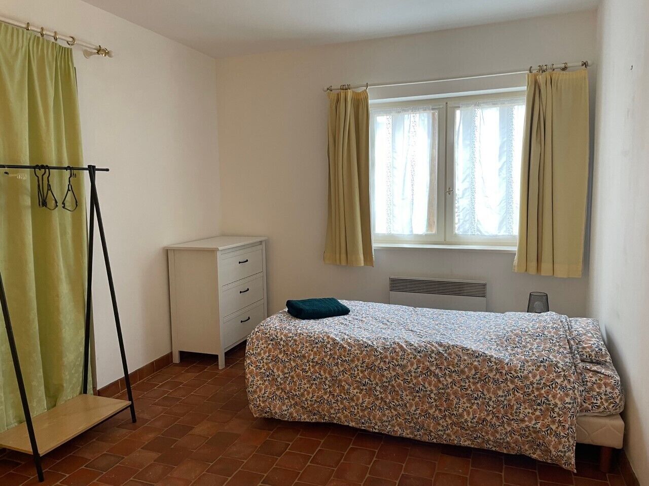 A bedroom with a bed, a dresser, a radiator, and a window with curtains.