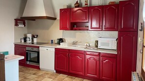 Une cuisine avec des placards rouges, un évier blanc, un four à micro-ondes et une machine à café.
