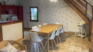 Un coin repas avec une table en bois et des chaises blanches, une cuisine rouge avec des placards et un escalier.