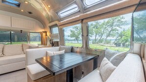 Een modern interieur van een camper, met een eethoek, zitplaatsen en grote ramen met uitzicht op een groen landschap.