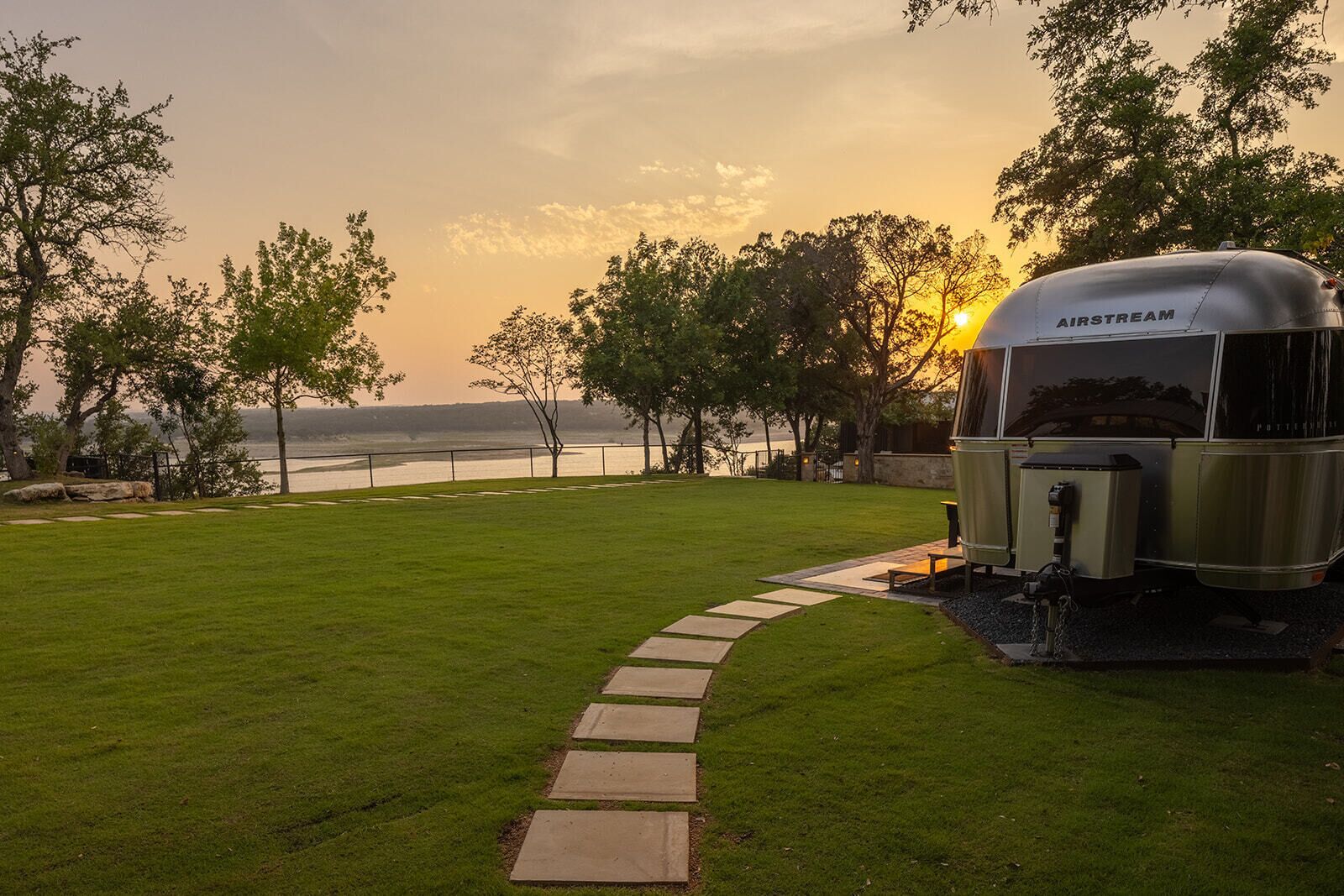 Una caravana de la marca 'AIRSTREAM' estacionada en un área cubierta de césped, con un camino de piedra que conduce a ella.