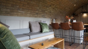 A cozy living area with a grey sofa, a wooden coffee table, and a kitchen in the background. - Hare's View Underground House (Rhayader)