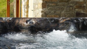A stone building with a wooden door and a hot spring area. - Hare's View Underground House (Rhayader)