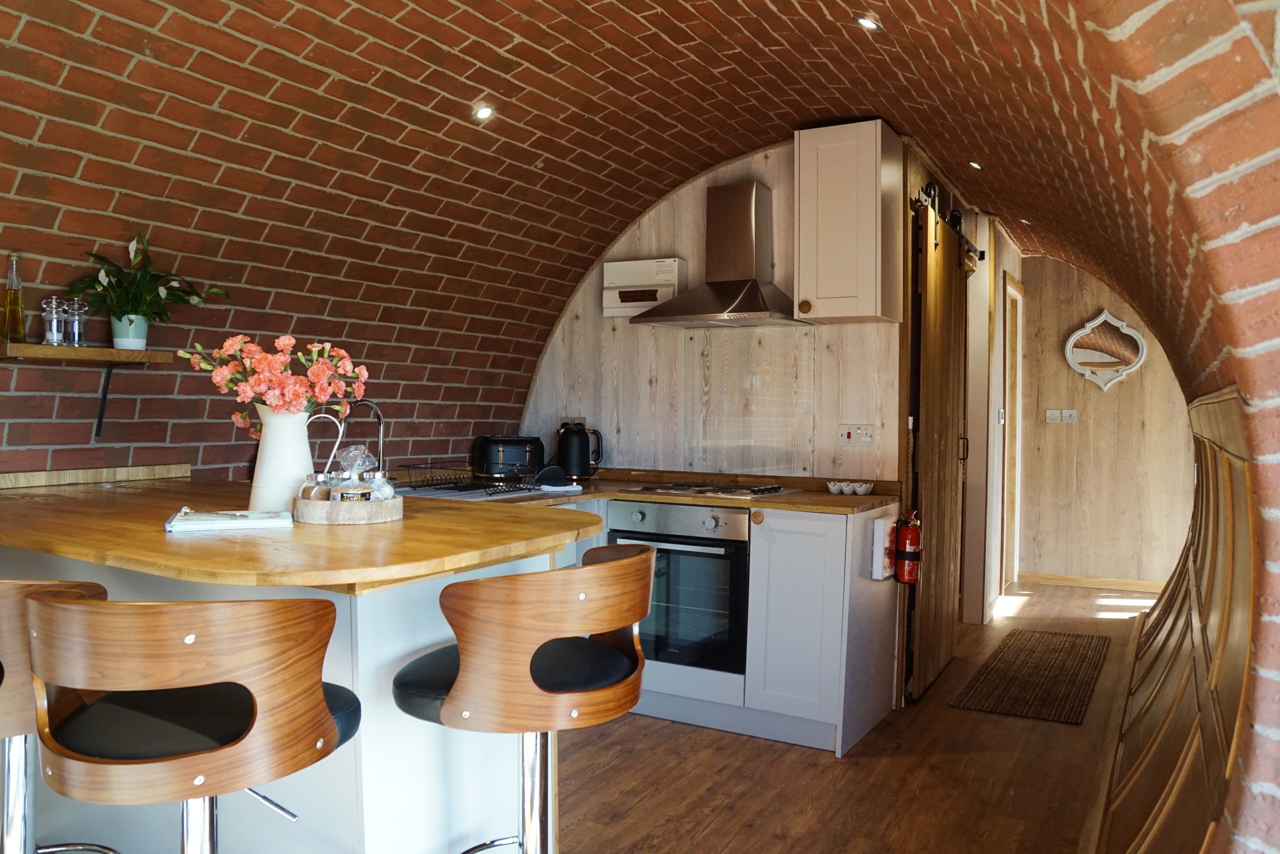 A kitchen with a brick ceiling, wooden cabinets, a stove, and bar stools.