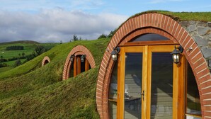 A series of brick-arched structures with wooden doors and windows, set on a grassy hill with a clear sky.