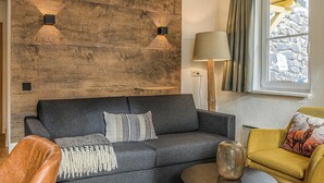 Un soggiorno moderno con un divano grigio scuro, una parete d'accento in legno, una lampada e una finestra con tende.