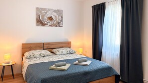 Een net opgemaakt bed met een blauwe quilt, twee kussens, een bedlampje en een aan de muur hangend kunstwerk.