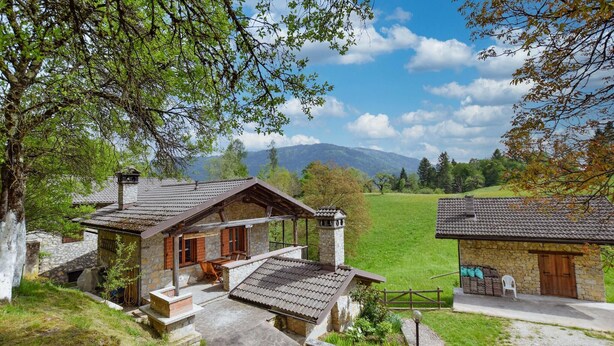Un bâtiment en pierre doté d’une terrasse en bois et offrant une vue sur un champ verdoyant et des montagnes.