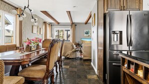 A kitchen with a large refrigerator, wooden cabinets, and a dining area with chairs and a table. - Stylish Chalet with Hot Tub and Jacuzzi! (Lake Arrowhead)