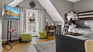 A cozy loft bedroom with a TV, bunk bed, desk, chair, and a view of a lake through a window. - Stylish Chalet with Hot Tub and Jacuzzi! (Lake Arrowhead)