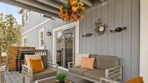 A covered outdoor patio with a sofa, a small table, and a hanging flower arrangement. - Stylish Chalet with Hot Tub and Jacuzzi! (Lake Arrowhead)