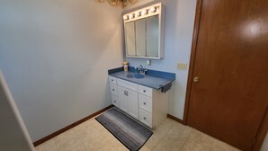 Une salle de bain avec un meuble-lavabo, un évier, un miroir et une porte.