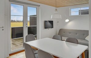 Enjoy a peaceful retreat with a sliding glass door leading to a grassy field view, a dining table, comfortable sofa, and flat-screen TV.