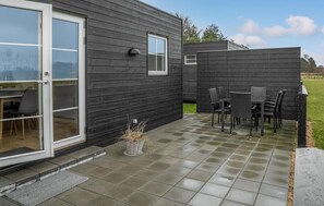 Relax on the patio with a table and chairs, surrounded by lush greenery and a serene lawn.