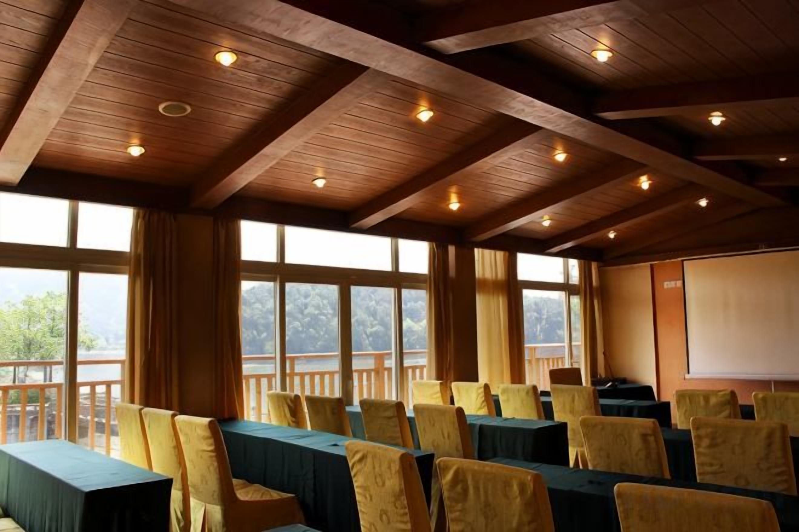 A conference room with tables and chairs, large windows, and a projector screen.