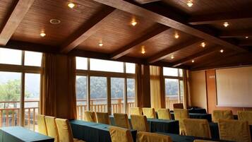 A conference room with tables and chairs, large windows, and a projector screen.