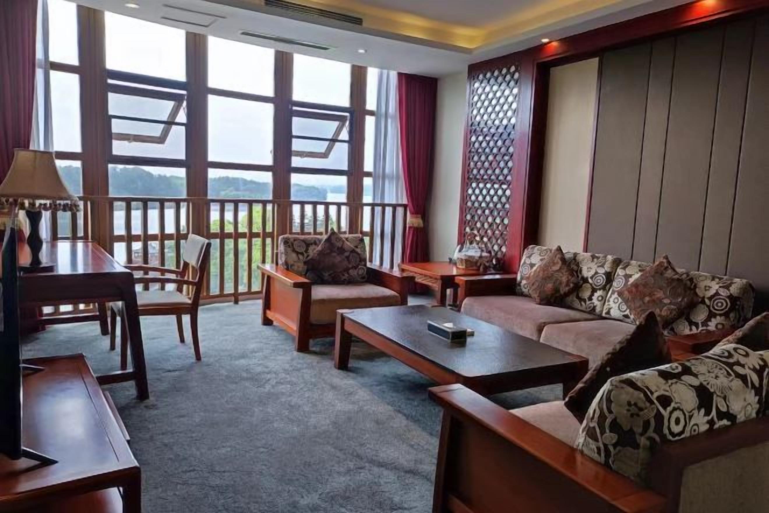 Una habitación con sofá, sillas, una mesa de centro, lámpara y vistas amplias a través de grandes ventanas.