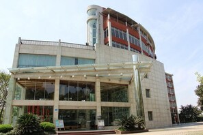 Un hotel de varios pisos con fachada de vidrio, entrada cubierta y exterior rojo y blanco.
