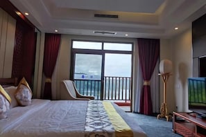 Una habitación de hotel con cama, sillón, televisión y balcón con vistas.