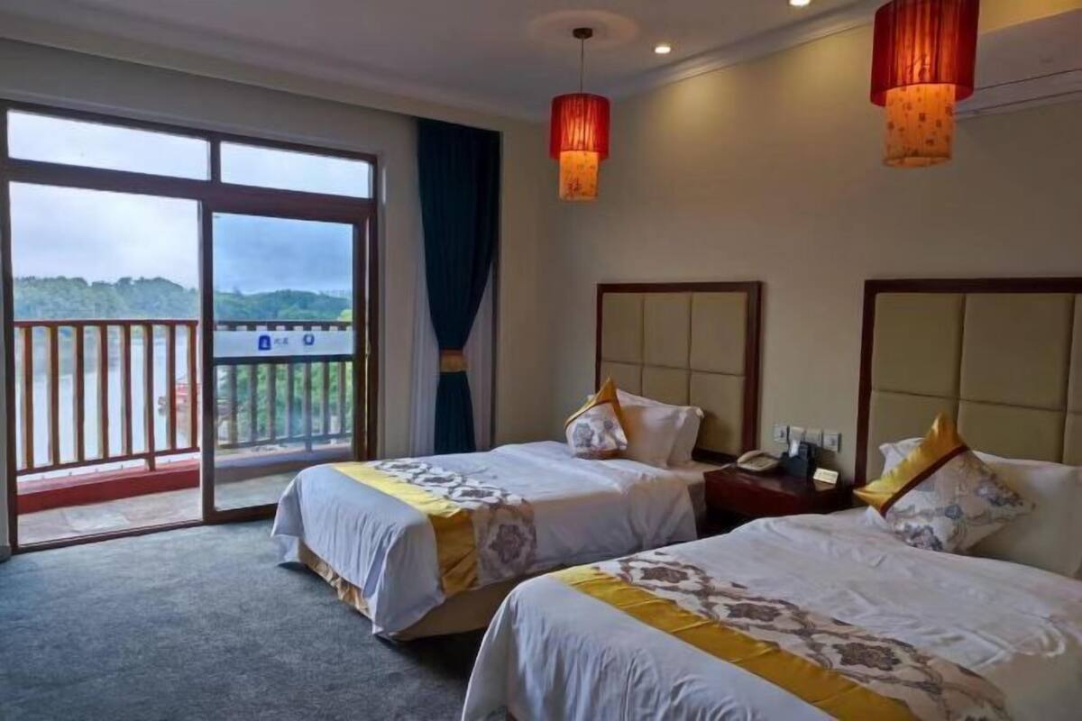 A hotel room with two beds, a balcony, and a view of the outdoors.