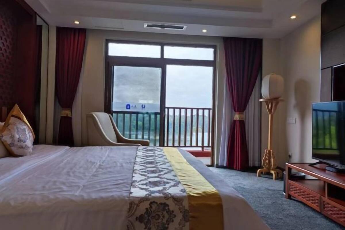 A hotel room with a bed, a television, a chair, and a balcony with curtains.