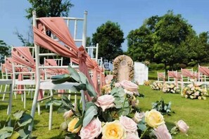 Un salón de bodas con filas de sillas, arreglos florales y un arco central.