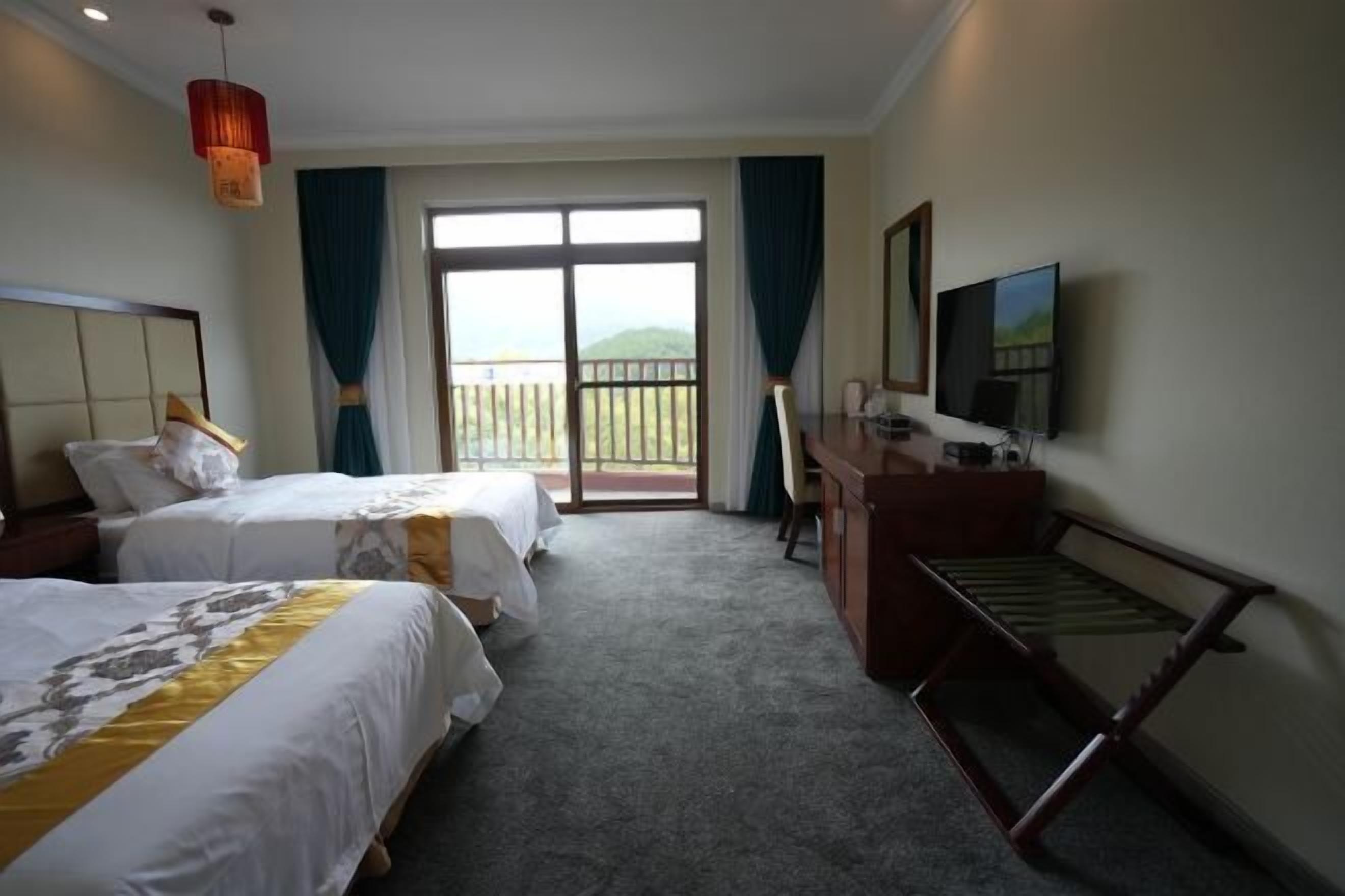 A hotel room with two beds, a desk, a television, and a balcony with a view.