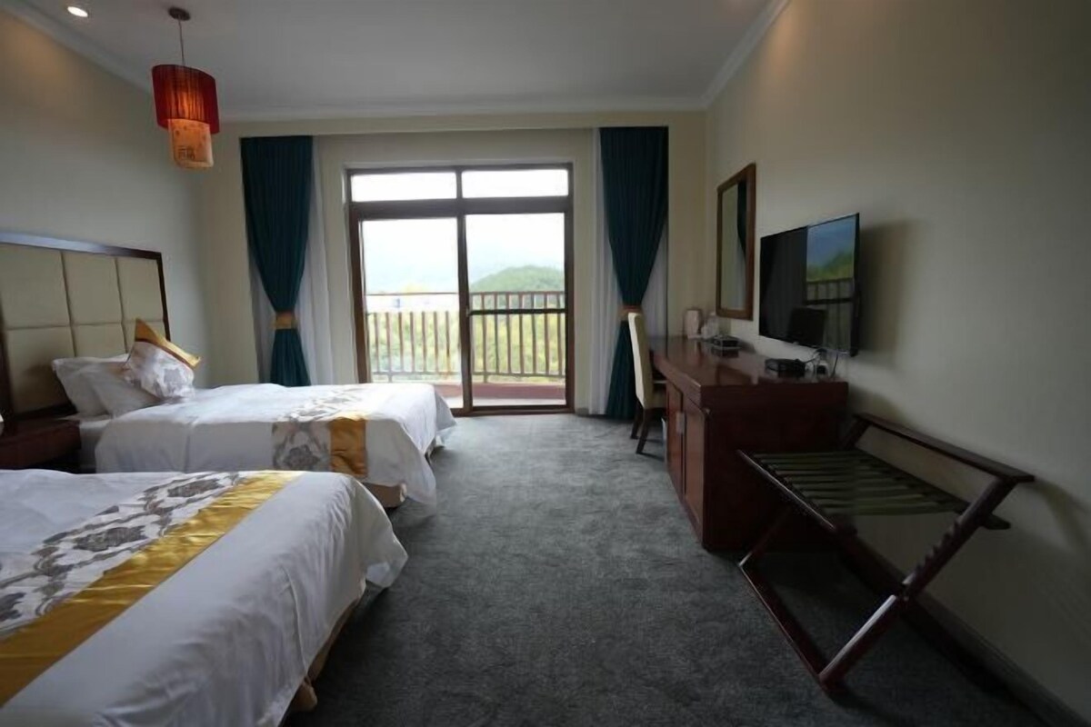 Habitación de hotel con dos camas, un escritorio, una televisión y un balcón con vistas.