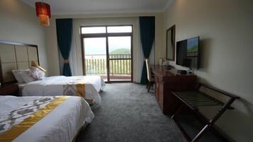 A hotel room with two beds, a desk, a television, and a balcony with a view.