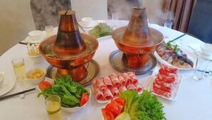 A dining table with two copper hot pots, various dishes including vegetables and meats, and a glass of drink. - Longshui Lake Dalong Bay Hotel (Chongqing)